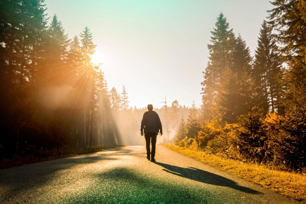 Mann spaziert auf einer Landstraße im Wald