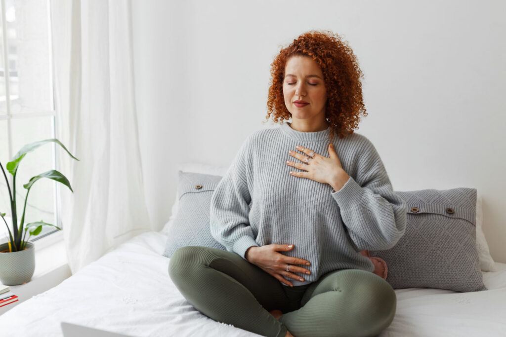 Frau sitzt auf dem Bett und macht Pranayama-Atemübungen