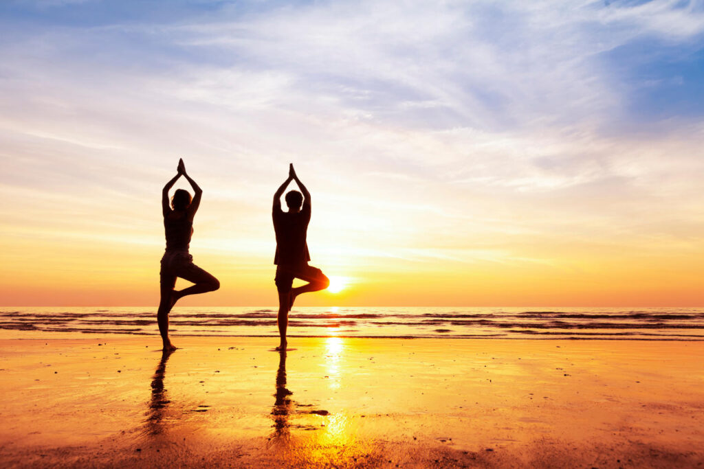 Zwei Personen praktizieren Yoga an einem Strand
